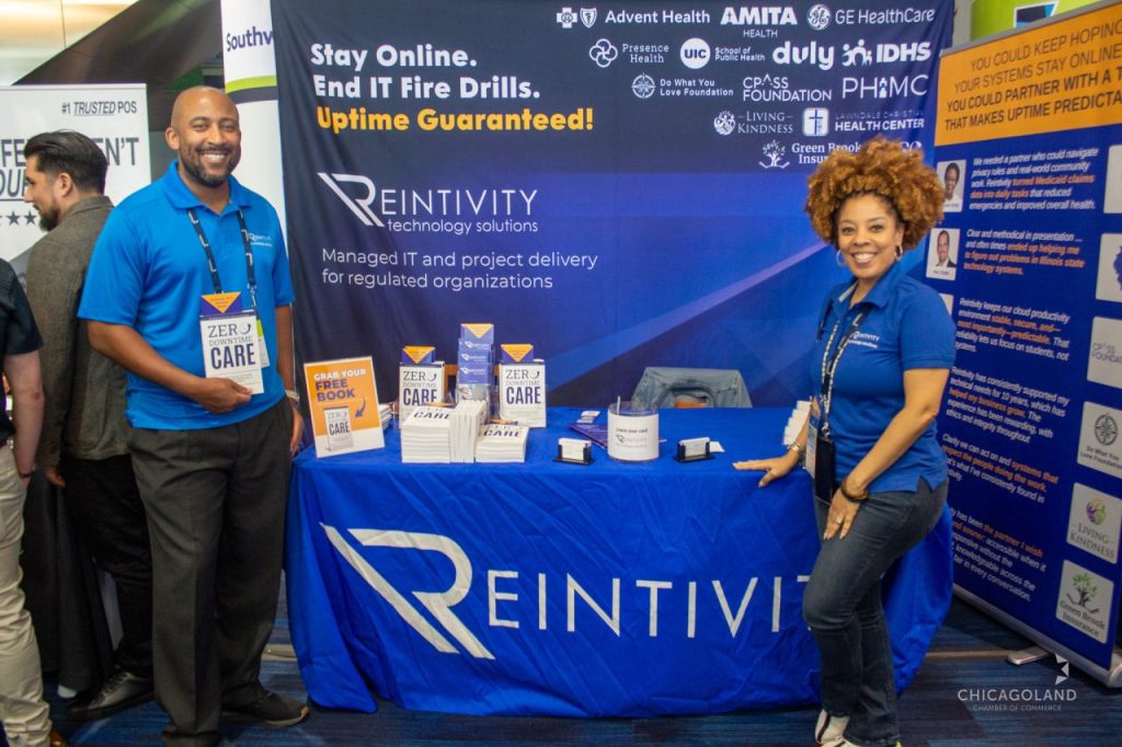 Reintivity team members at Booth 52 during The Exchange 2026, holding and displaying copies of “Zero-Downtime Care,” engaging attendees on reducing IT fire drills, improving system reliability, and creating more predictable operations.