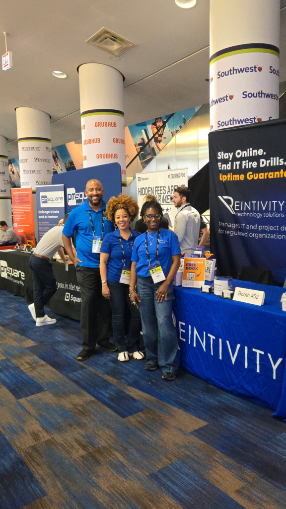 Reintivity team members standing at Booth 52 during The Exchange 2026 at Soldier Field, speaking with attendees about reducing IT fire drills, improving security, and streamlining workflows for more stable and predictable operations.