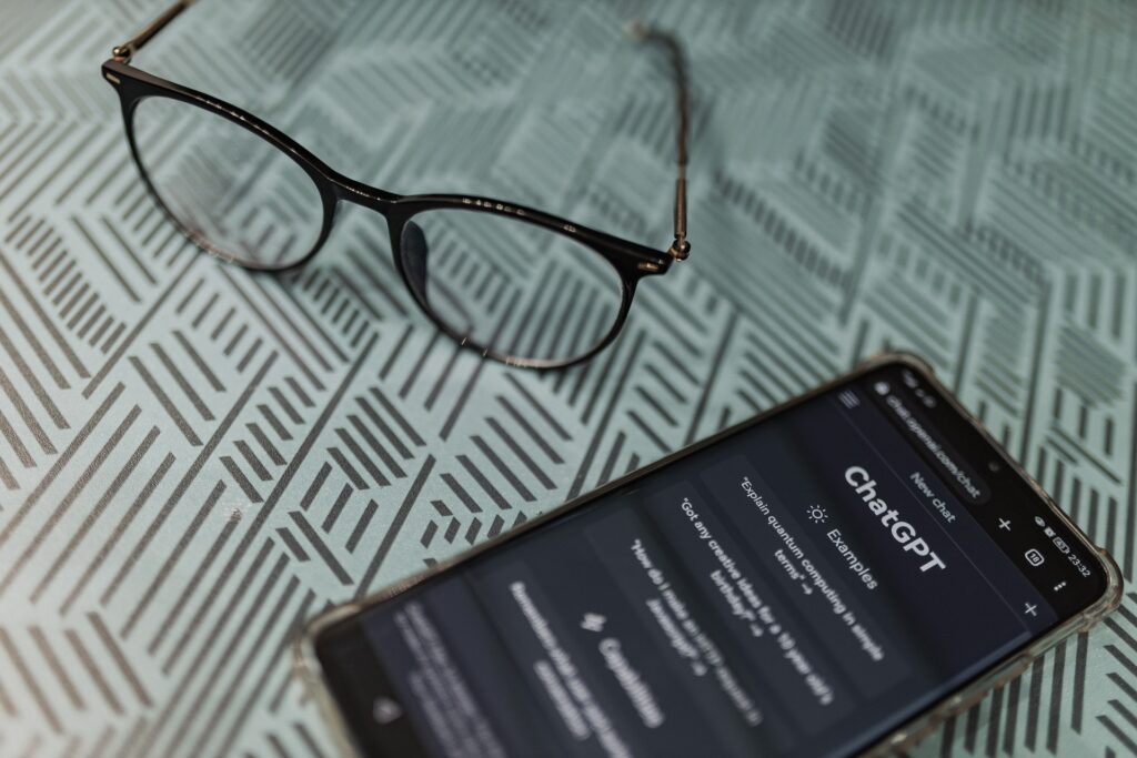 eye glasses on table next to smartphone displaying AI tool ChatGPT.
